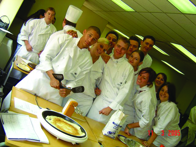 Group of culinary students wearing white uniforms and chef hats in a kitchen setting. - International Hotel School