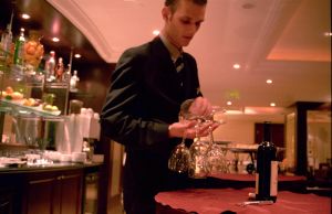 Bartender arranging glassware on a red table in a hotel setting with drinks in the background. - International Hotel School