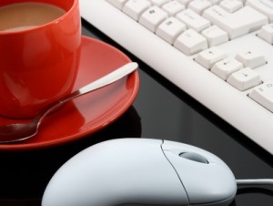 Red coffee cup with a spoon beside a computer mouse and keyboard on a black surface. - International Hotel School