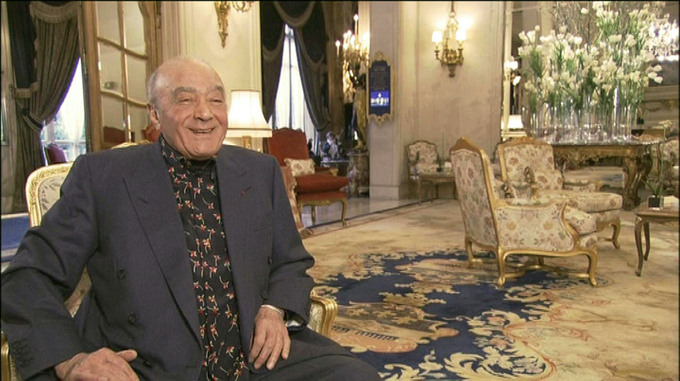 A man in a dark suit with a patterned shirt sitting in a luxurious hotel lobby with ornate decor. - International Hotel School