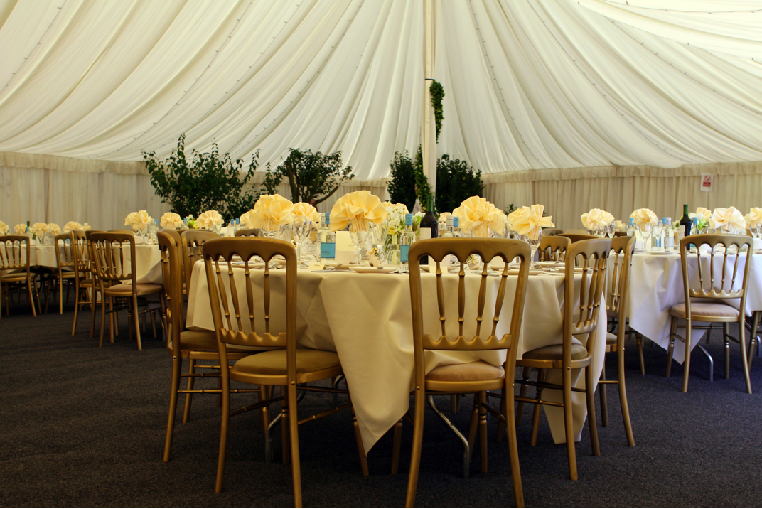 A dining area featuring round tables with cream-colored tablecloths and floral centerpieces under a draped ceiling. - International Hotel School