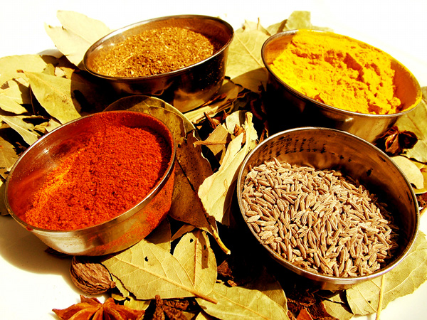 Four bowls containing different spices including cumin, turmeric, and red chili powder on a bed of dried leaves. - International Hotel School