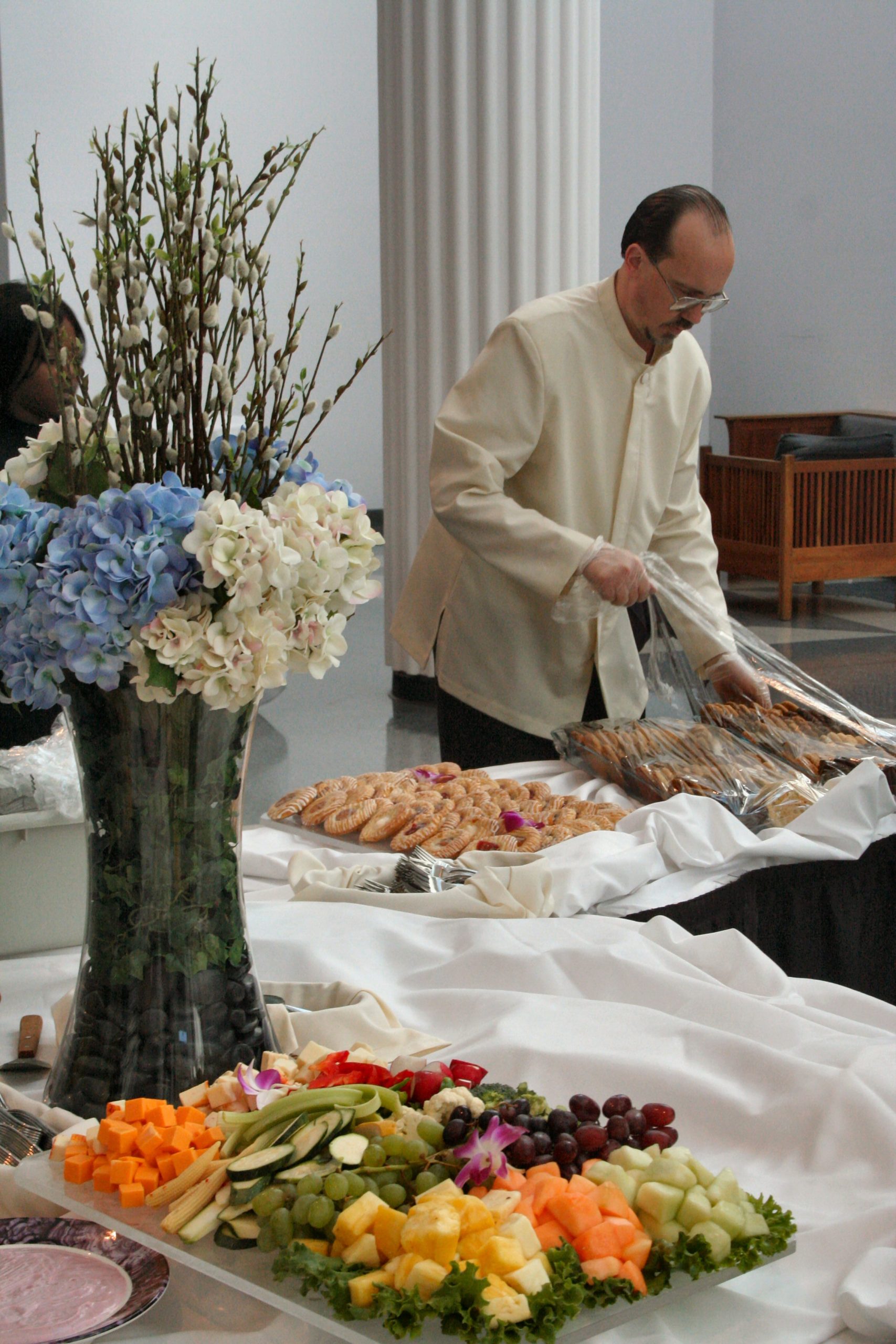 A catering professional arranging food items on a table with a floral centerpiece. - International Hotel School