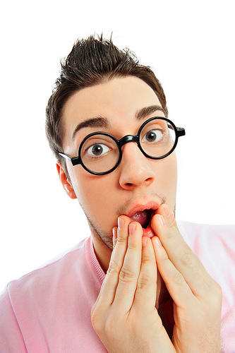 A young man with glasses showing a surprised expression with his hands on his mouth. - International Hotel School