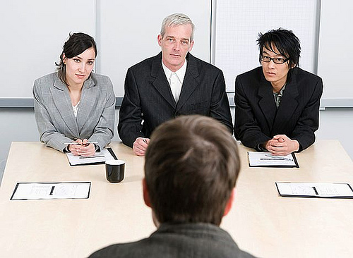 Three interviewers seated at a table during a job interview, looking at the candidate. - International Hotel School