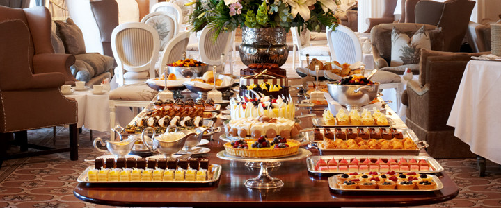 A dessert table featuring a variety of cakes, pastries, and sweets arranged elegantly on silver trays. - International Hotel School