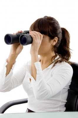 A woman in a white shirt looking through binoculars while seated at a desk. - International Hotel School