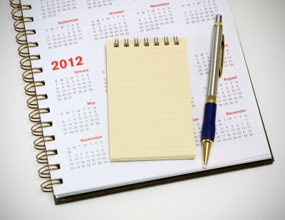 Spiral bound notebook with blank pages next to a pen on a calendar for the year 2012. - International Hotel School