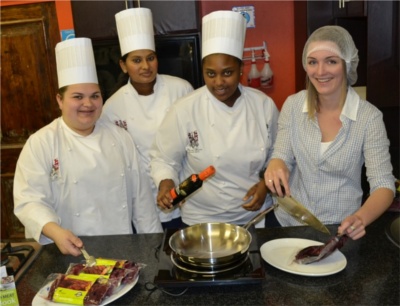 Four culinary students in white chef uniforms preparing food in a kitchen setting. - International Hotel School