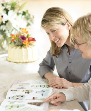 Two women discussing event planning while looking at a brochure and a cake in front of them. - International Hotel School