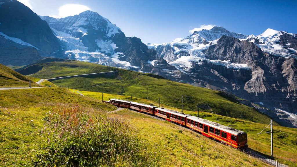 Jungfrau Railway train traveling through the Swiss Alps with mountains and greenery in the background. - International Hotel School