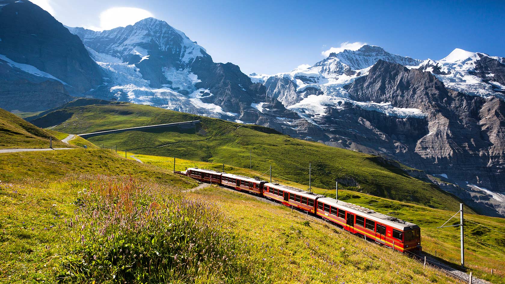 Jungfrau Railway train traveling through the Swiss Alps with mountains and greenery in the background. - International Hotel School