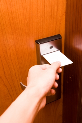 A hand holding a key card while inserting it into a hotel door lock mechanism. - International Hotel School