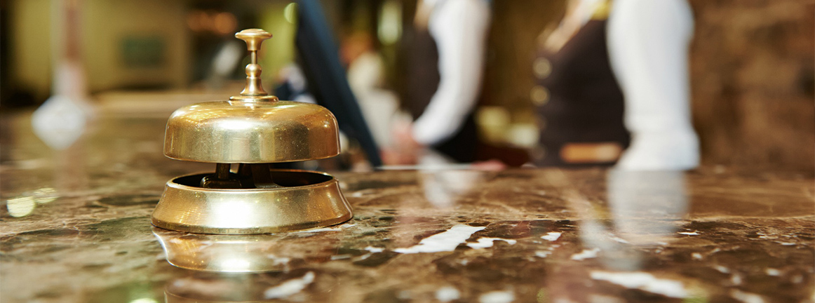Brass reception bell placed on a marble hotel counter with staff in the background. - International Hotel School