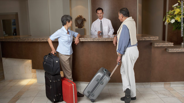 Two guests interacting with a hotel receptionist at the front desk with luggage. - International Hotel School