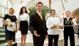 Five hospitality professionals in formal attire, including a chef, waiter, and service staff, posing together indoors. - International Hotel School