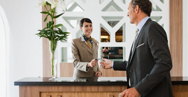 A hotel receptionist handing a key card to a guest at the front desk. - International Hotel School