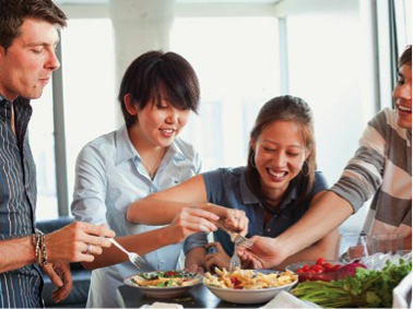 Four friends enjoying a meal together, sharing dishes at a table. - International Hotel School