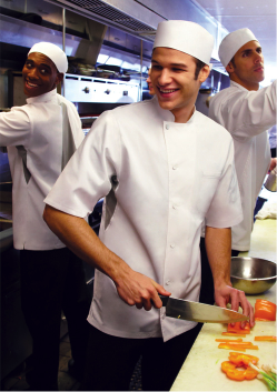 Culinary students in a kitchen preparing food, one chopping vegetables and others working in the background. - International Hotel School