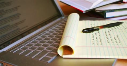 A laptop with a notepad and pen placed on a desk, showing handwritten notes. - International Hotel School