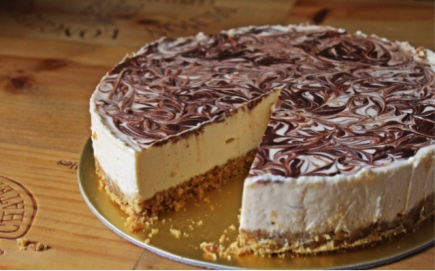 A round chocolate swirl cheesecake with a slice removed, displaying a creamy texture and graham cracker crust. - International Hotel School