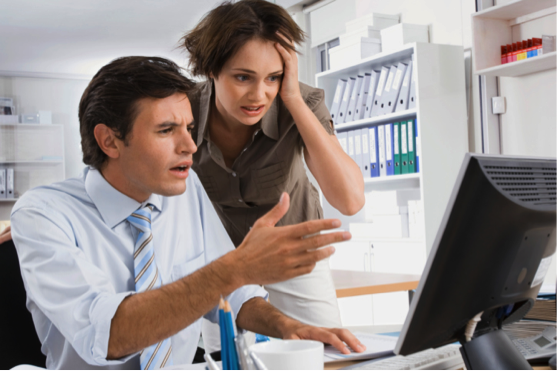 Two business professionals, a man and a woman, discussing something on a computer screen in an office setting. - International Hotel School