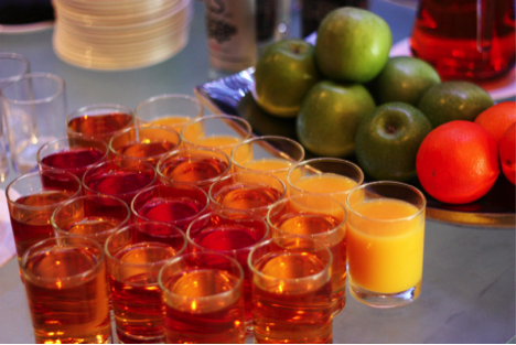 Variety of fruit juices in clear glasses alongside fresh apples and oranges on a table. - International Hotel School