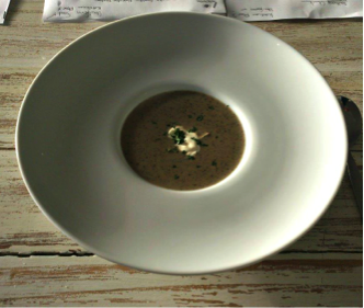Bowl containing a serving of mushroom soup with a garnish of cream and herbs. - International Hotel School