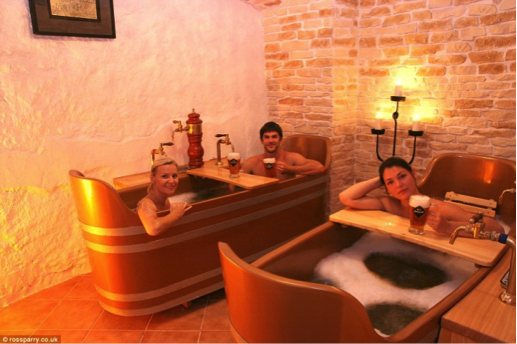 Three individuals relaxing in wooden bathtubs with taps and beer mugs in a softly lit room. - International Hotel School
