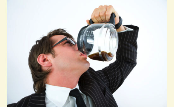 Man in a suit drinking coffee directly from a glass carafe with a serious expression. - International Hotel School
