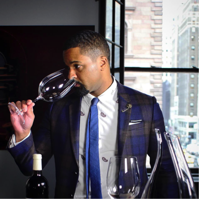 Man in a plaid suit holding a large wine glass while examining its contents. - International Hotel School
