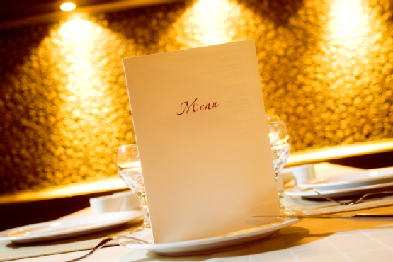 A restaurant menu placed on a table with elegant tableware and soft lighting in the background. - International Hotel School