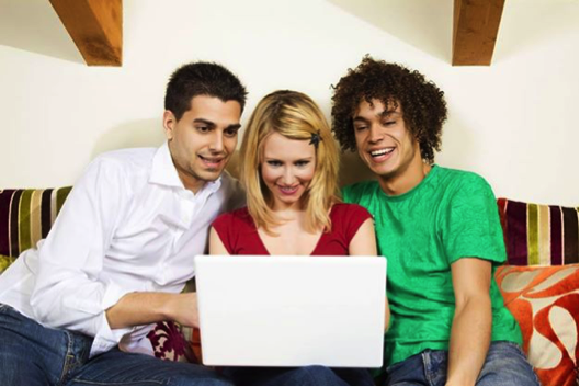 Three individuals, two males and one female, engaged with a laptop while sitting on a couch. - International Hotel School
