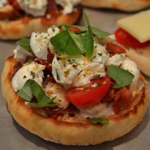 Pizza muffins topped with mozzarella, tomatoes, and fresh basil leaves on a baking tray. - International Hotel School