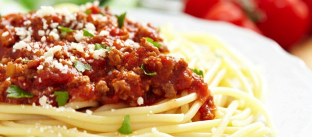 Plate of spaghetti topped with Bolognese sauce and garnished with herbs. - International Hotel School