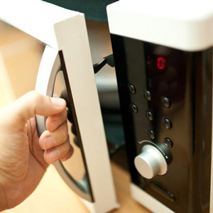 A hand opening the door of a microwave oven with a digital display and control panel. - International Hotel School