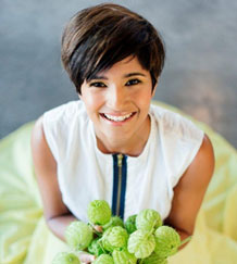 A woman with short hair smiling while holding a bunch of fresh green vegetables. - International Hotel School