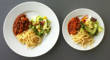 Two plates containing spaghetti with sauce and mixed salad on a gray surface. - International Hotel School