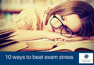 A student wearing glasses resting on a stack of books while studying at a desk. - International Hotel School