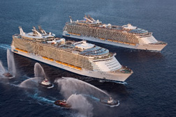 Two large cruise ships sailing in open water with tugboats spraying water. - International Hotel School