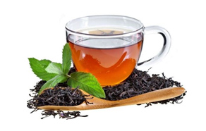 A clear glass cup filled with black tea, surrounded by loose black tea leaves and a sprig of mint. - International Hotel School