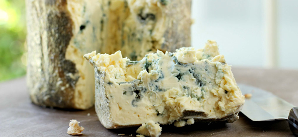 A wedge of blue cheese with a knife, showcasing its creamy texture and blue veins. - International Hotel School