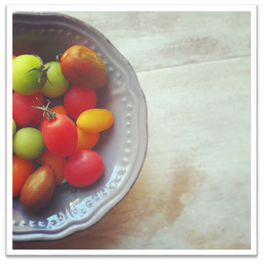 A bowl filled with various cherry tomatoes in different colors including red, yellow, and green. - International Hotel School