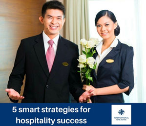 Two hospitality professionals in formal attire holding flowers, standing together indoors. - International Hotel School