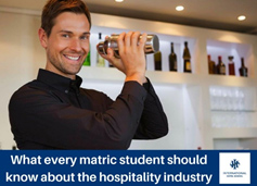 Man smiling while shaking a cocktail shaker in a hospitality environment with bottles in the background. - International Hotel School