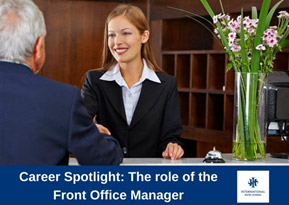 A front office manager assisting a guest at a hotel reception desk with flowers in the background. - International Hotel School