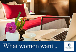 A hotel room featuring a laptop on a desk and an orchid plant on a bedside table. - International Hotel School