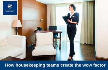 Housekeeping staff member standing in a hotel room holding a clipboard and wearing a uniform. - International Hotel School