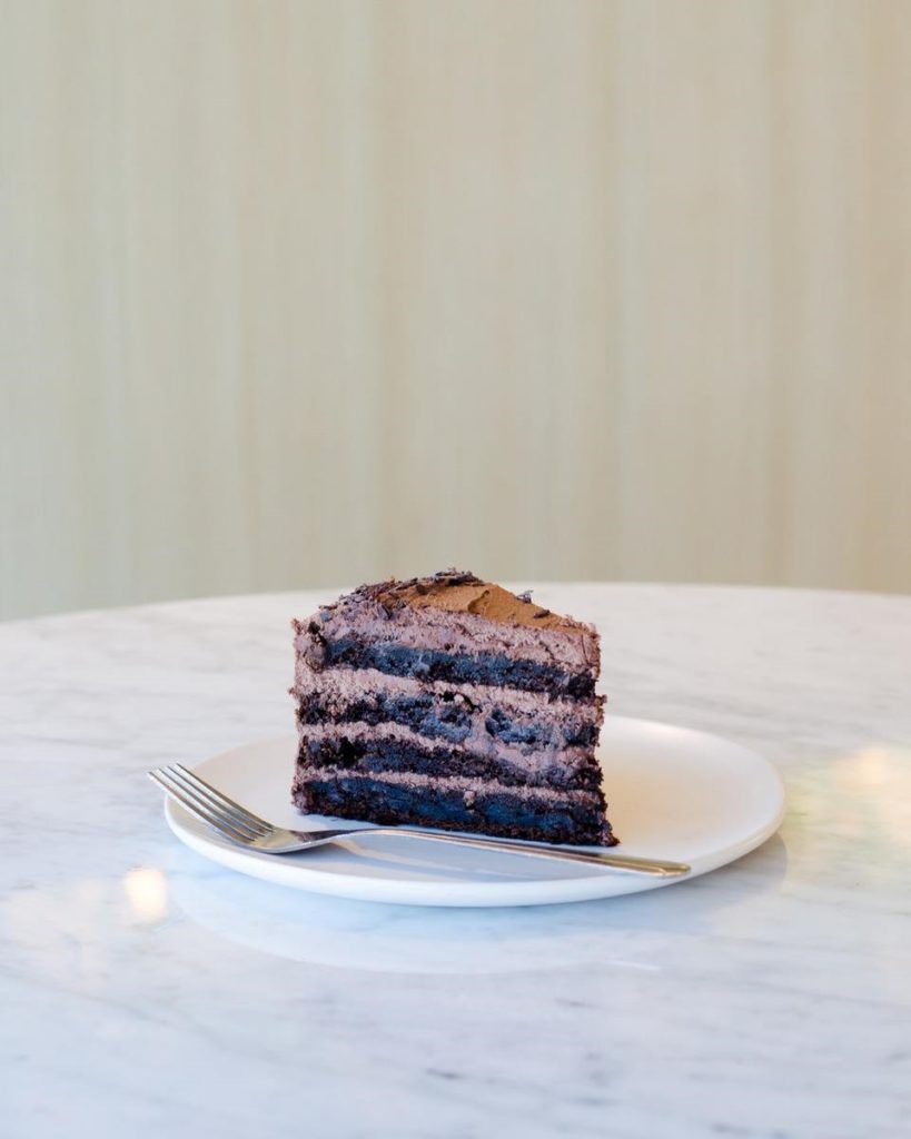 A slice of chocolate cake with layers and chocolate frosting on a white plate. - International Hotel School