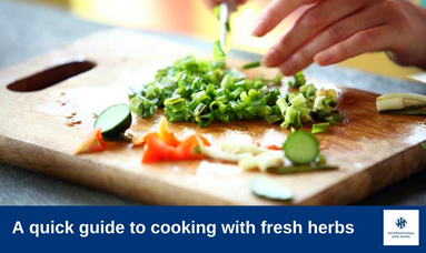 Chopped green onions and other fresh herbs on a wooden cutting board with a hand preparing them. - International Hotel School
